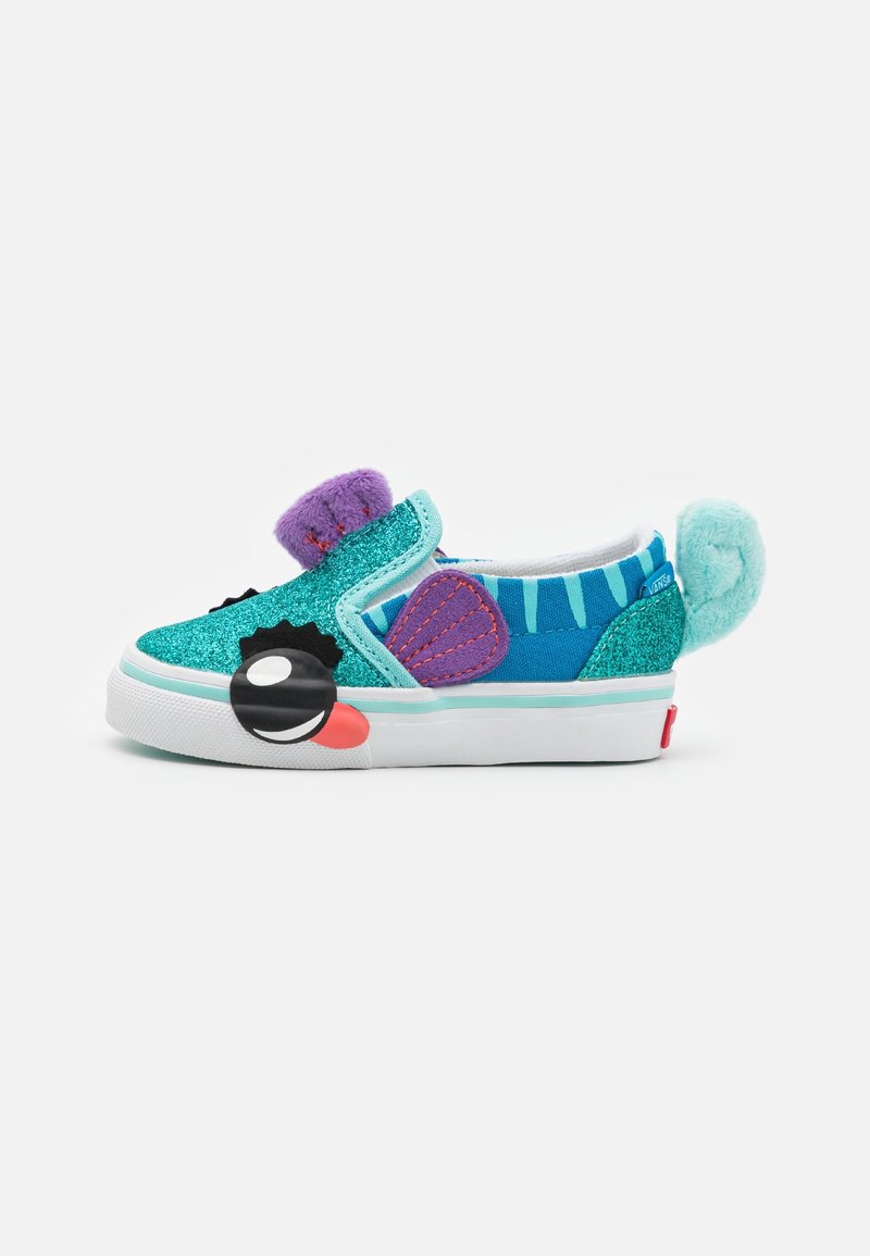 Zapatilla de deporte turquesa sin cordones con acentos decorativos, incluyendo texturas moradas y turquesas, una cara de dibujo animado negra y pompones multicolores.