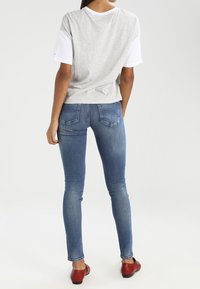 Camiseta gris de manga corta con detalles en blanco, combinada con jeans ajustados azules y zapatos planos rojos. Tejido suave y diseño ajustado.