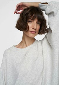 Felpa di colore grigio chiaro con scollo rotondo, vestibilità casual e polsini a costine. Presenta una cucitura sottile con il numero "10" sul petto.