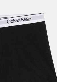 Μαύρο ύφασμα με λευκή ελαστική ζώνη μέσης που φέρει το όνομα της μάρκας "Calvin Klein" σε μαύρο κείμενο.