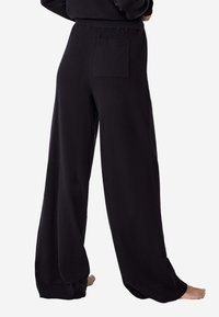 Černé kalhoty s širokým zakončením vyrobené z měkké tkaniny s žebrovaným pasem a našitou kapsou na zadní straně. Hladký povrch a volný střih.