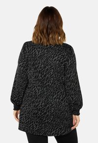 Černá tunika s texturovaným šedým vzorem, s dlouhými rukávy a elastickými manžetami a volným střihem.