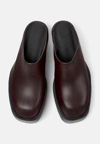 Pari di scarpe slip-on in pelle marrone scuro con punte quadrate arrotondate e solette nere imbottite con il logo "CAMPER" impresso.