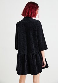 Rochie cu imprimeu de leopard negru, cu tiv adunat, mâneci trei sferturi și textură moale. Prezintă o croială lejeră și un decolteu rotund.