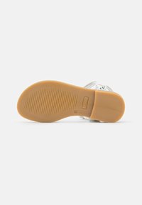 Przezroczyste gumowe sandały z teksturowaną podeszwą, z białą cholewką w zielone kwiatowe wzory i brązową podeszwą dla lepszej przyczepności.