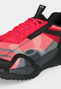 Φωτεινό ροζ και μαύρο αθλητικό παπούτσι Under Armour με παχύ πέλμα, μαύρο λουράκι και έντονο λογότυπο στην πλευρά και στην τριχιά της γλώσσας.