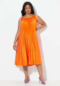 Vestido naranja con pliegues, sin mangas, de largo a la rodilla, hecho de una tela suave, con un escote redondo y una textura sutil.