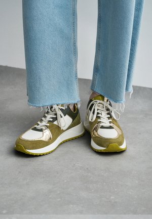 Sneakers with a mix of olive green suede and mesh, golden accents, and white laces. Features a thick white sole and textured details.