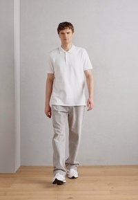 White polo shirt, light gray pants, and white sneakers. Simple design, short sleeves, smooth texture, functional collar, and minimal accents.