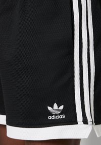 Zwarte sportshorts van geweven stof, met witte zijstrepen en een witte afwerking, en een klein wit Adidas-logo op de zoom.