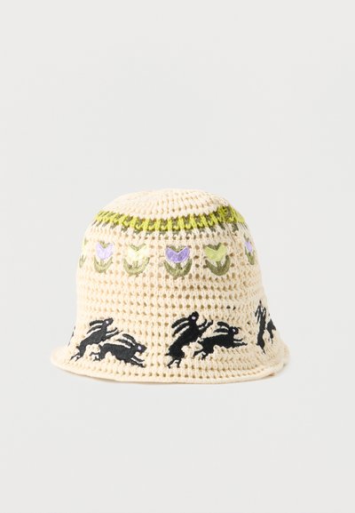 Πλεκτό μπεζ καπέλο τύπου μπακιρέ με κεντητά μοβ και πράσινα λουλούδια κοντά στην κορυφή και μαύρα κουνέλια που τρέχουν γύρω από το γείσο.