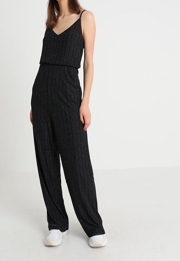 Černý overal s tenkými ramínky, žebrovanou strukturou a volnými širokými nohavicemi. Doplněno o bílé tenisky pro kontrast.