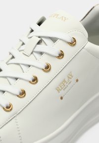 Hvit sneaker med gulløyelets og "REPLAY siden 1981" merkingen på siden, med hvite lisser på en tykk såle.