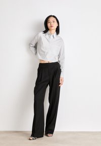 Camicia corta button-up grigio chiaro con taschino, abbinata a pantaloni neri a gamba larga a vita alta e sandali bianco e nero.