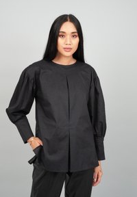 Black long-sleeve shirt with a round neckline, pleated front, and tapered sleeves. Made of smooth fabric with a structured fit.