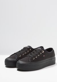 Schwarze Stoffschuhe mit einer strukturierten Gummisohle, runder Zehenpartie, Metallösen und flachen Schnürsenkeln; verfügt über ein kleines Logodetail in der Nähe der Ferse.