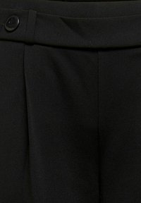 Černé kalhoty na míru s vysokým pasem, detailem poutka na pásek, přední záhybout a jediným černým knoflíkem na levé straně.