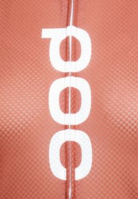 Sarkans rakstains audums ar baltu "poc" logo, ar redzamu tekstūru un dūrieniem pa centru.