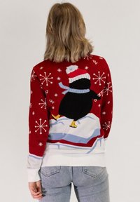 Red knitted sweater featuring a penguin on an ice patch with blue scarf, white cuffs, and snowflake patterns throughout.