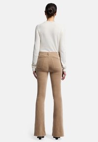 Beige flare corduroy broek met achterzakken en een hoge taille, gecombineerd met een romige trui van gebreid materiaal. Zachte textuur en aansluitend ontwerp.