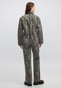 Completo giacca e pantaloni con stampa leopardata, con colletto nero, tessuto texturizzato e silhouette aderente. Stivali neri con suola spessa completano il look.
