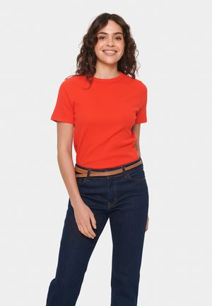 Red ribbed short-sleeve top paired with dark blue denim jeans and a brown belt. The top has a round neckline and fitted silhouette.