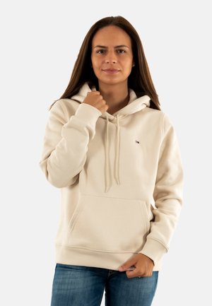 Hoodie beige avec capuche à cordon, poche avant et détails de manches côtelées. Présente une petite étiquette de logo sur la poitrine gauche.