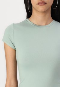 Tricou mint verde, ajustat, cu mâneci scurte și decolteu rotund, fabricat dintr-un material neted și elastic. Detalii de cusătură vizibile la umeri.