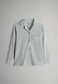 Lys grå langærmet natdragts bluse med hvid piping på kraven, manchetterne og brystlommen, lagt fladt på en grå baggrund.