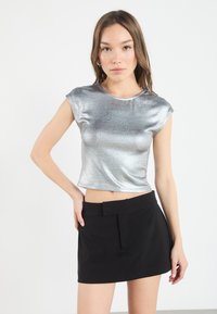 Top corto metálico plateado con mangas cortas tipo capa, combinado con una falda mini negra de talle alto que presenta una cinturilla plana y detalles de pliegues.