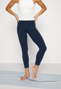 Leggings blu navy con vita alta, realizzati in tessuto elasticizzato, con dettagli delle cuciture e taglio alla caviglia. Abbinati a un top bianco.