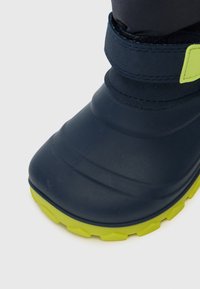 Botte en caoutchouc bleu foncé avec un dessus texturé, dotée d'une sangle verte et d'une semelle striée pour une meilleure adhérence.