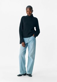 Zwarte ribgebreide coltrui gecombineerd met lichtblauwe wijde jeans. De outfit heeft een ontspannen pasvorm en zachte texturen.