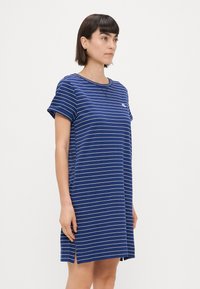 Abito a t-shirt a righe blu navy con maniche corte, scollatura rotonda e fessure laterali; presenta righe orizzontali bianche e un piccolo logo.