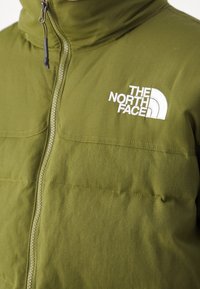 Veste zippée vert olive à col montant, avec un logo "The North Face" blanc brodé sur la poitrine gauche.