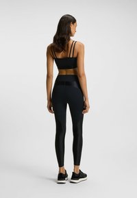Czarny sportowy biustonosz z cienkimi ramiączkami i czarne legginsy z wysokim stanem oraz teksturowanymi panelami, zestawione z czarnymi butami sportowymi.