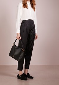 Biała bluzka z długim rękawem, czarne spodnie plisowane z wysokim stanem, czarne loafersy oraz czarna skórzana torebka na ramię z złotymi elementami.