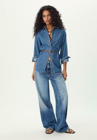 Camicia in denim con vita aderente e design a bottoni, abbinata a jeans a gamba larga sbiaditi. Colore blu uniforme con una consistenza morbida.