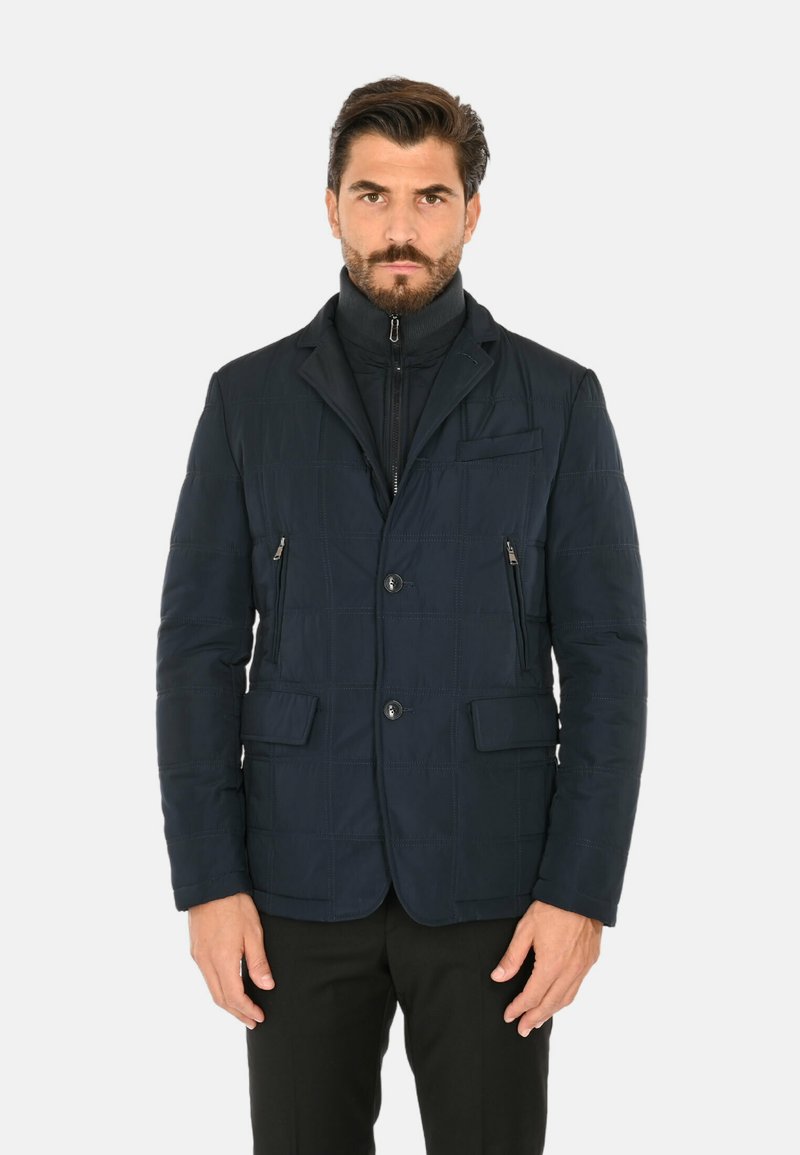 Giacca trapuntata blu navy con colletto alto, chiusura frontale con bottoni, due tasche con zip e tessuto strutturato con un sottile motivo a griglia.