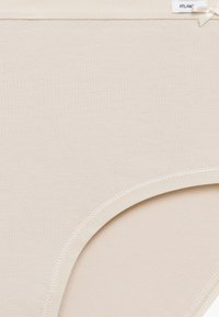 Beżowa bawełniana bielizna o gładkiej fakturze, z przeszytym brzegiem i małą satynową kokardką na etykiecie w talii.