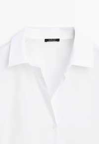 Chemise blanche à col boutonné avec un col pointu classique et une étiquette visible à l'intérieur de l'encolure.