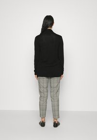 Svart långärmad topp med en avslappnad passform, i kombination med grå rutig byxor och svarta skor. Slät textur och minimalistisk design.