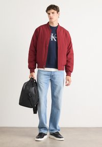 Red bomber jacket, navy crewneck sweatshirt, light blue jeans, black leather sneakers, and a black tote bag held in hand.