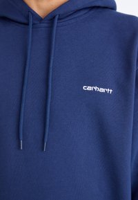 Navy blue hoodie with drawstrings, featuring a small white Carhartt logo on the chest. Fabric appears soft with a smooth texture.