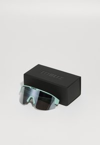 Sonnenbrille mit einem mintgrünen Rahmen und großen verspiegelten Gläsern, die auf einer schwarzen Box mit erhabenem Logo liegen. Rechteckige Form mit strukturierten Akzenten.