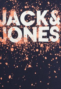 T-shirt navy con grande testo bianco "JACKS & JONES" e motivo spruzzato in corallo. Materiale in cotone con una texture liscia.