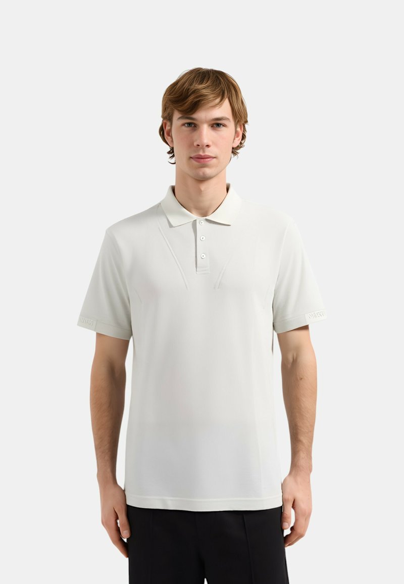 Polo shirt beige chiaro con colletto, maniche corte e dettagli di cucitura sottili. Presenta un logo sulla manica sinistra. Texture liscia.