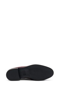 Zapato burdeos con parte superior de ante texturizado y suela de goma negra. La suela tiene un patrón uniforme para tracción y presenta el logo de la marca en relieve.