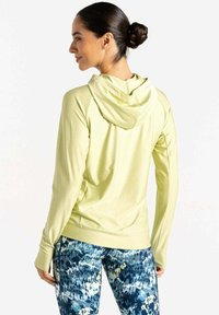 Helles gelbes Kapuzenoberteil mit langen Ärmeln und lässiger Passform, kombiniert mit leggings im blauen und grünen Muster, das ein sportliches Design zeigt.