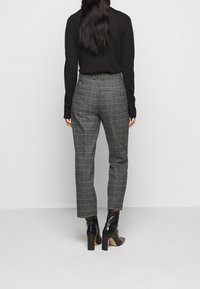 Haut à manches longues noir associé à un pantalon à carreaux gris, avec une coupe ajustée. Des bottes à talons noires complètent la tenue.